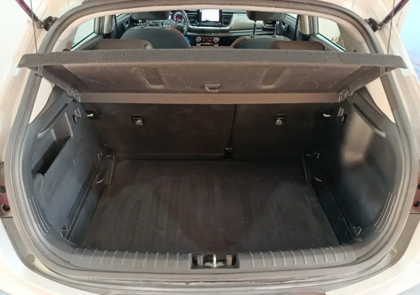 Coffre ouvert d'une KIA Stonic gris clair vue de l'arrière, montrant l'intérieur spacieux et la tablette de séparation.