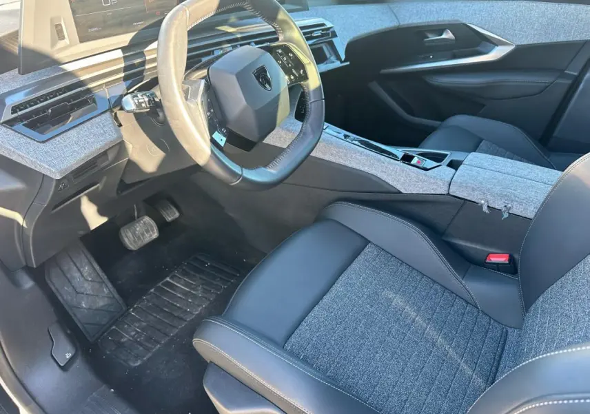 Intérieur avant droit du Peugeot 3008 Hybrid 145 Allure 2025, sièges tissu et cuir gris, tableau de bord moderne avec volant compact.