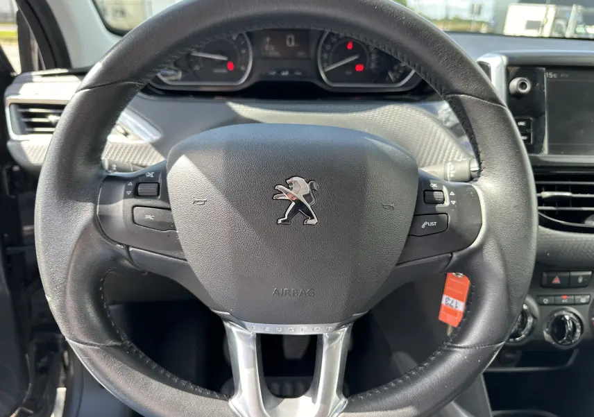 Volant en cuir noir avec logo Peugeot au centre, tableau de bord et console centrale du Peugeot 2008 gris 2019 visibles en arrière-plan.