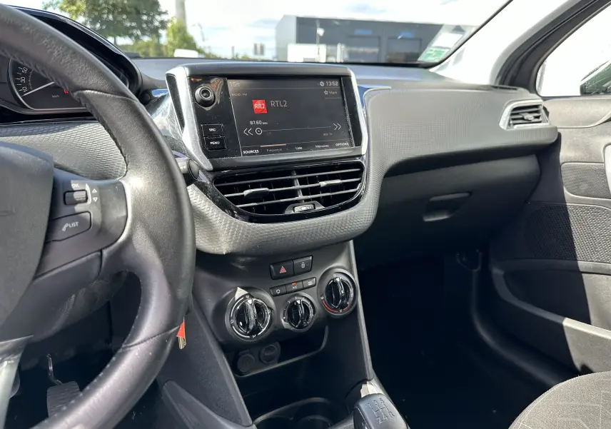 Vue intérieure côté conducteur du tableau de bord d'une Peugeot 2008 gris 2019 avec écran tactile et climatisation manuelle.