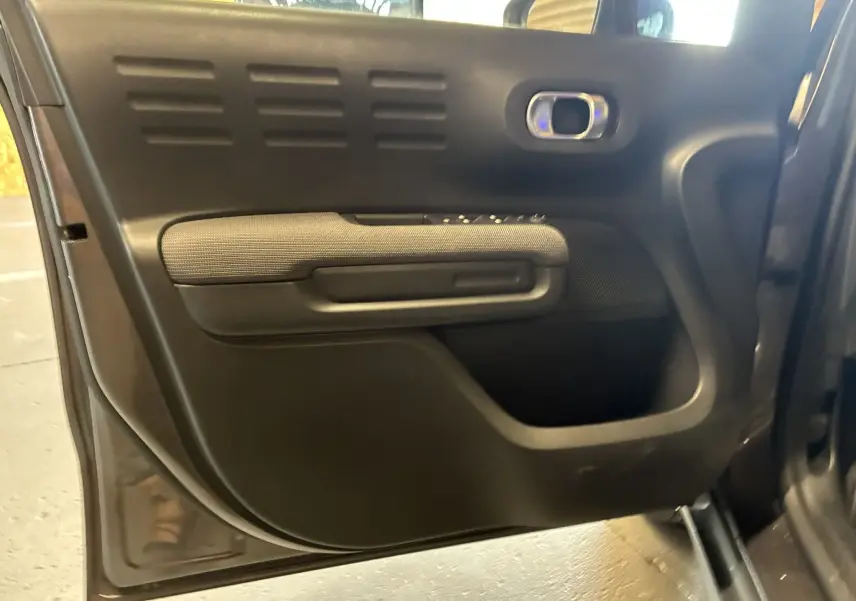 Gros plan sur la porte intérieure côté gauche du Citroën C3 Aircross gris platinium, avec accoudoir tissu gris et commandes électriques.