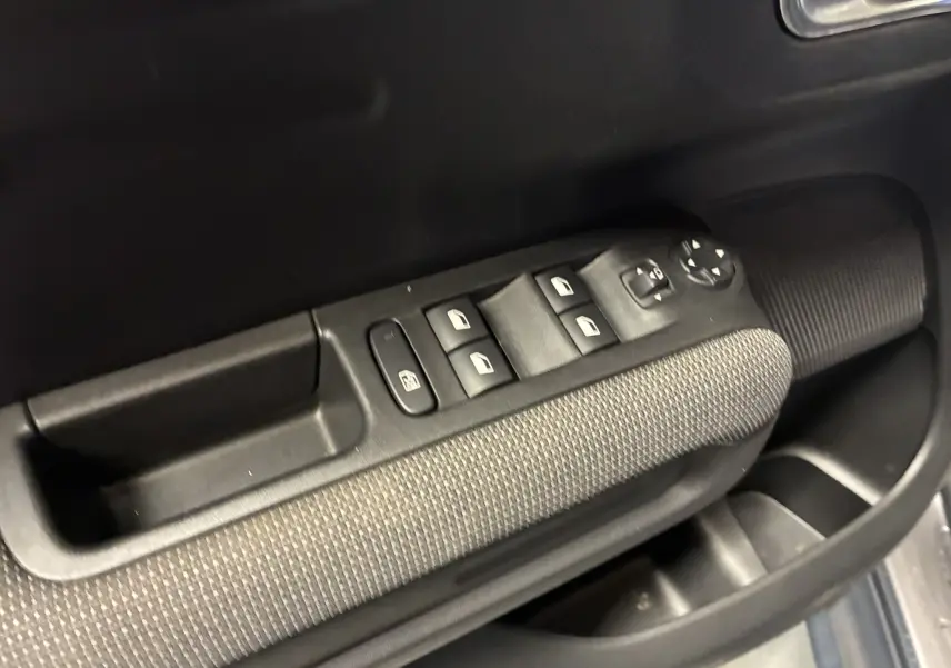 Gros plan sur la commande des vitres électriques côté conducteur avec accoudoir tissu gris noir dans une Citroën C3 Aircross 2023.
