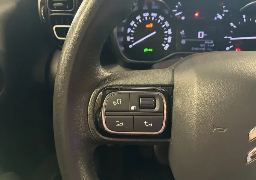 Gros plan sur les commandes multifonctions à gauche du volant cuir du Citroën C3 Aircross 2023, tableau de bord en arrière-plan.