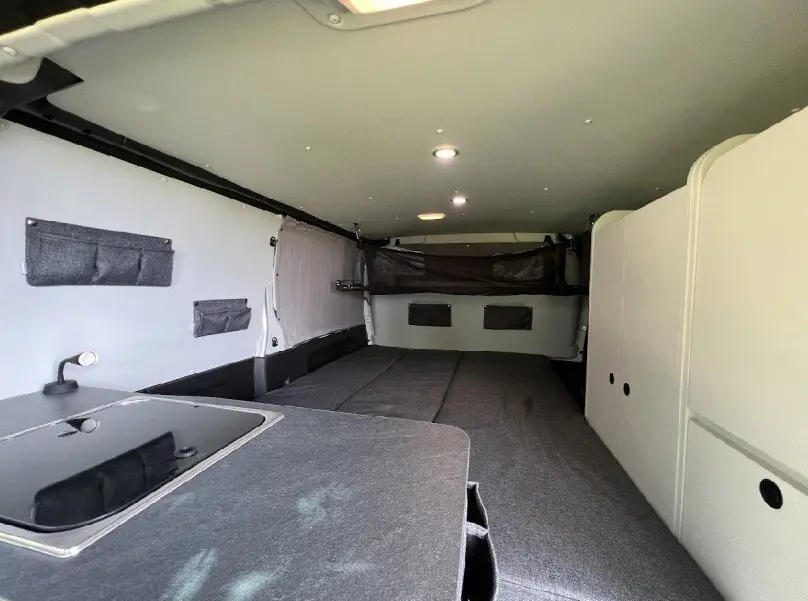 Intérieur du fourgon Renault Trafic gris, vue sur l'espace couchage et rangements avec éclairage LED au plafond.