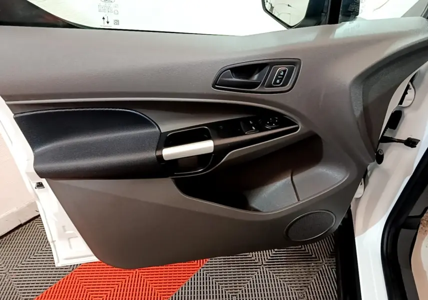Vue rapprochée de la porte avant gauche blanche du Ford Transit Fourgon, avec commandes de vitres et poignée noire.
