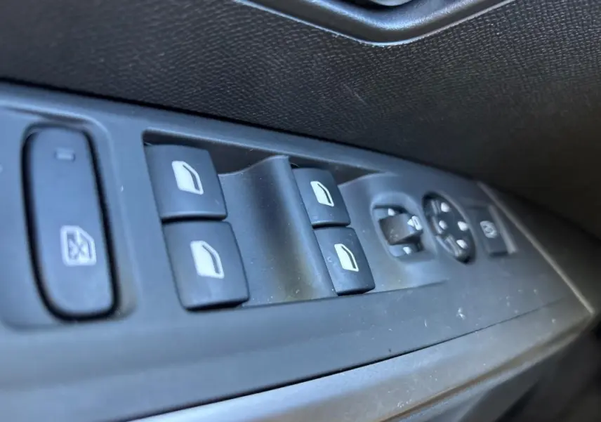 Gros plan sur les commandes des vitres électriques et rétroviseurs côté gauche d’un Peugeot 3008 gris 2025.