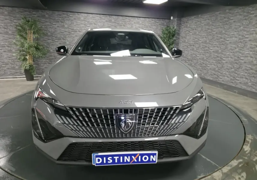 Vue avant d'une Peugeot 408 gris métallisé avec calandre verticale et logo lion distinctif, en showroom intérieur.