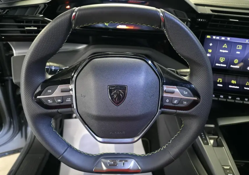 Volant cuir perforé noir avec surpiqûres vertes et logo GT, planche de bord et écran tactile Peugeot 408 hybride rechargeable.