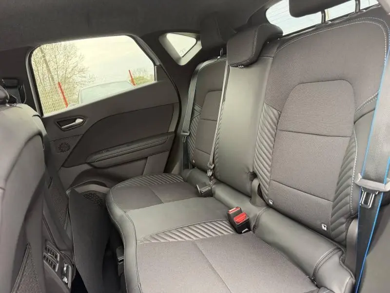 Vue intérieure arrière côté droit du Renault Captur 2026, sièges noirs avec surpiqûres bleues et ceinture de sécurité visible.