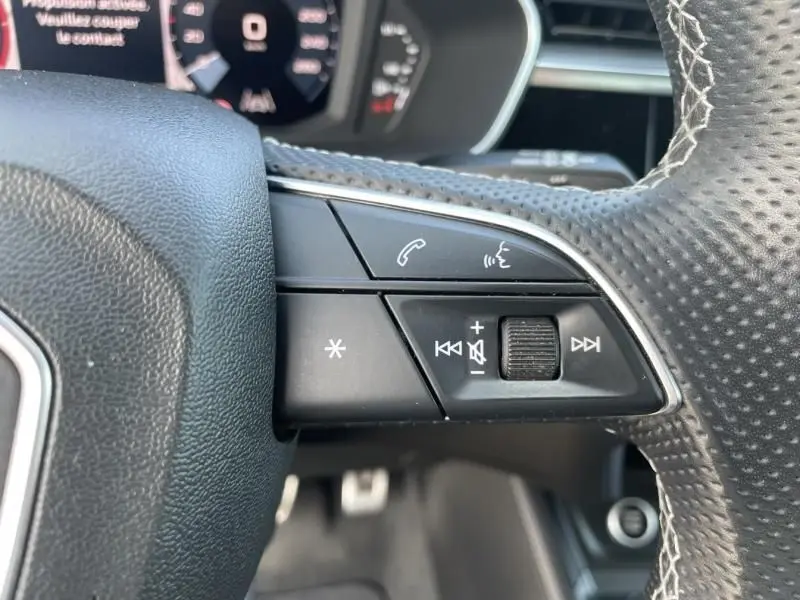 Gros plan sur les commandes audio et téléphone au volant perforé d'un Audi Q3 blanc 2021, version S-Line.
