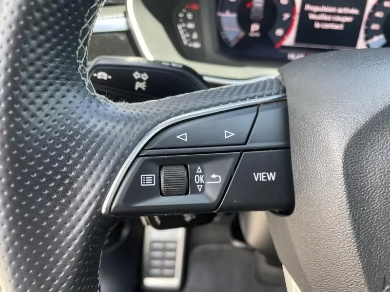 Gros plan sur les commandes gauche du volant perforé d'un Audi Q3 blanc 2021, version S-Line avec affichage numérique partiel.