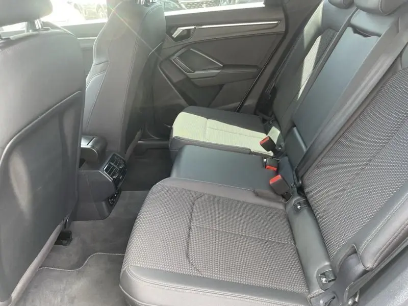 Vue latérale droite de l'intérieur arrière de l'Audi Q3 blanc 2021, sièges tissu gris et cuir noir avec accoudoir central.