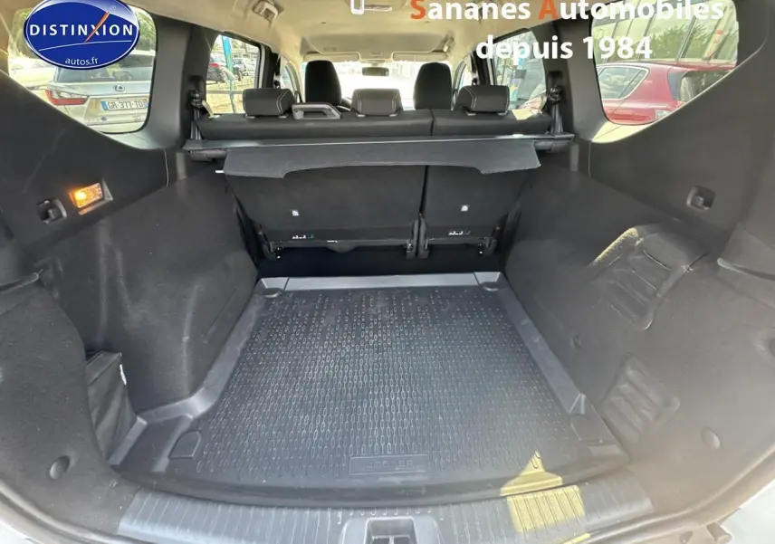 Coffre ouvert du Dacia Jogger blanc, vue intérieure arrière montrant la banquette rabattable et le tapis de coffre noir.