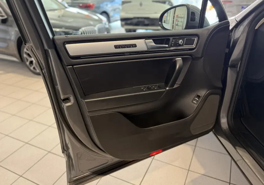 Porte avant gauche ouverte du Volkswagen Touareg gris foncé, montrant les commandes de vitres et le revêtement intérieur noir avec insert argenté.