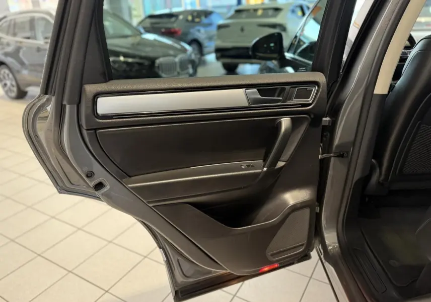 Porte arrière gauche ouverte du Volkswagen Touareg gris foncé, intérieur noir avec insert argenté et haut-parleur intégré.