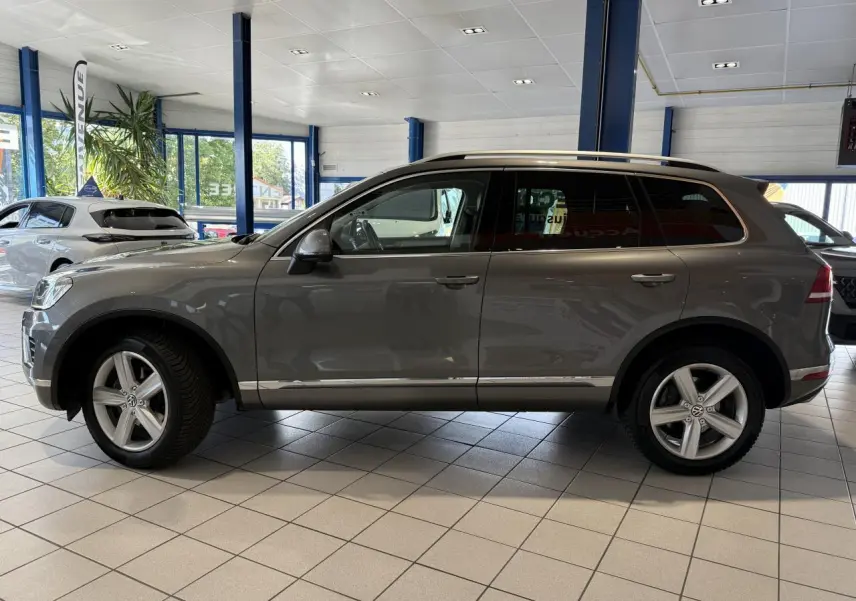 Volkswagen Touareg gris foncé vu de profil côté gauche, jantes alliage 19 pouces, intérieur showroom lumineux.