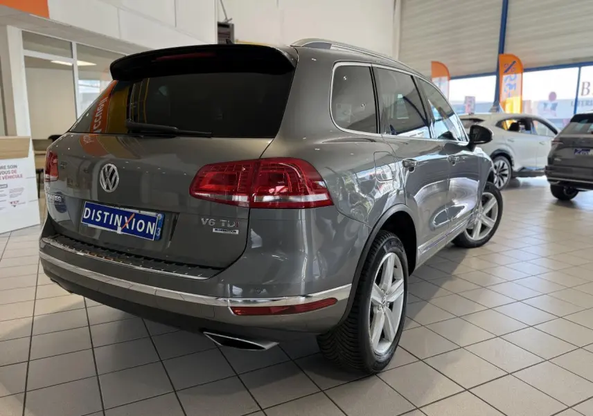 Volkswagen Touareg gris foncé en 3/4 arrière droit dans un showroom avec jantes alliage 19 pouces et vitres teintées.