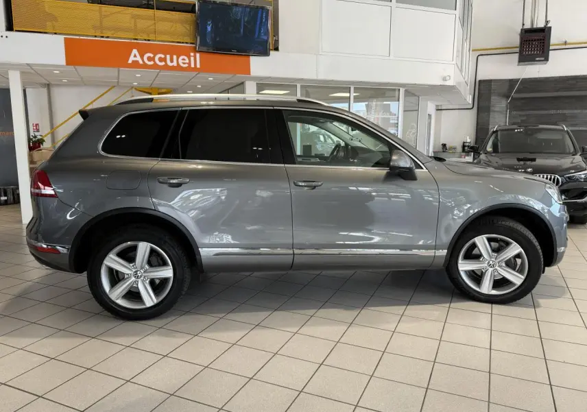 Profil côté droit d'un Volkswagen Touareg gris foncé 2017 en showroom, avec jantes alliage 19 pouces et vitres teintées.