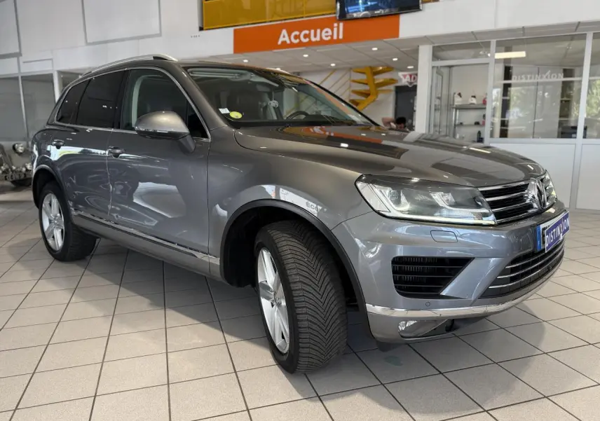 Volkswagen Touareg gris foncé vu en 3/4 avant droit dans un showroom avec éclairage intérieur.