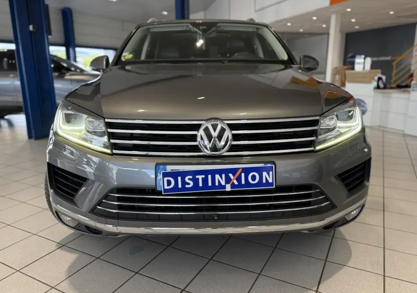 Vue de face du Volkswagen Touareg gris foncé avec phares allumés et calandre chromée en showroom.