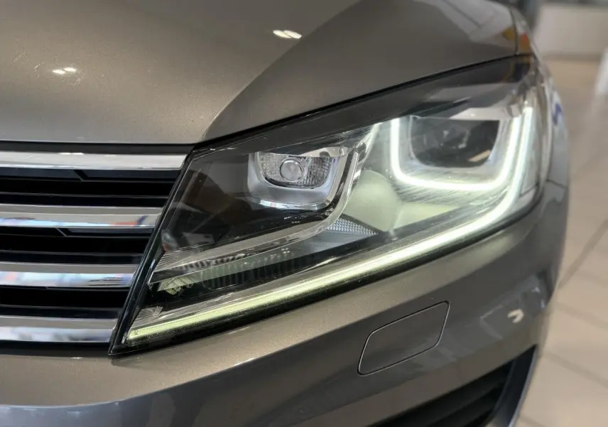 Gros plan sur le phare avant droit allumé d'un Volkswagen Touareg gris foncé, soulignant ses lignes modernes et LED distinctives.
