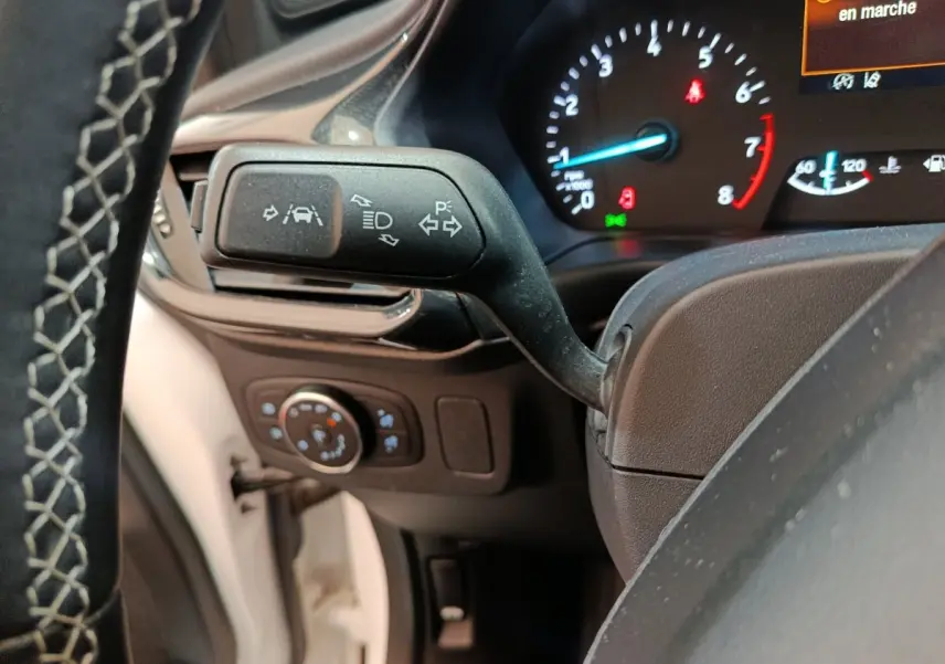 Gros plan sur la commande de clignotants et tableau de bord numérique du Ford Puma blanc, affichage en marche.