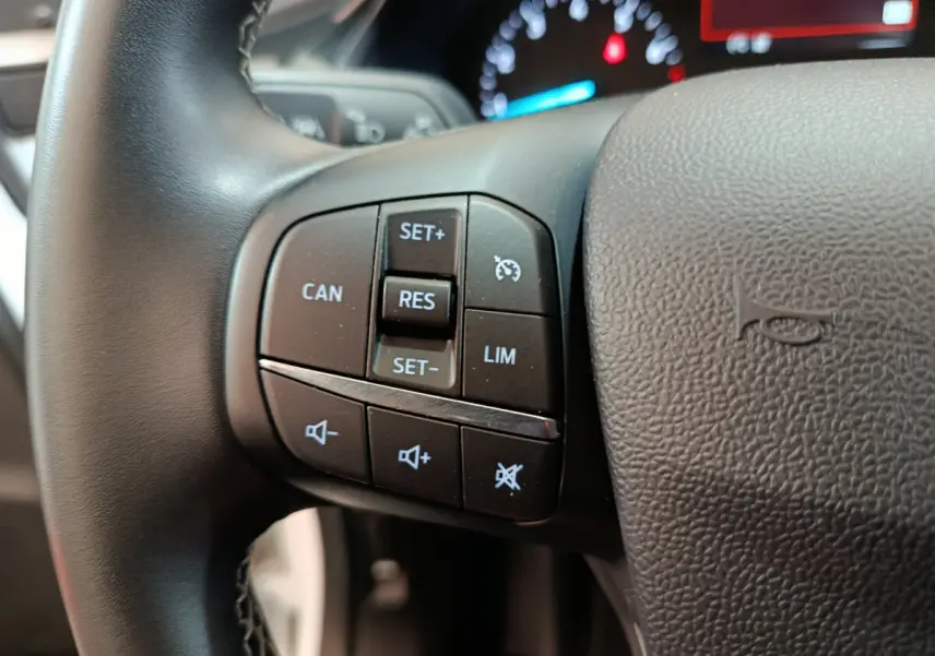 Gros plan sur les commandes au volant côté gauche du Ford Puma blanc 2022, avec affichage du tableau de bord en arrière-plan.