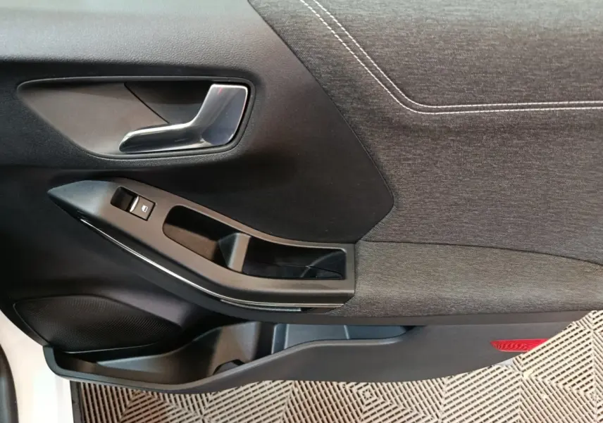 Gros plan sur la porte intérieure côté conducteur du Ford Puma blanc, montrant la poignée et les commandes de fenêtre.