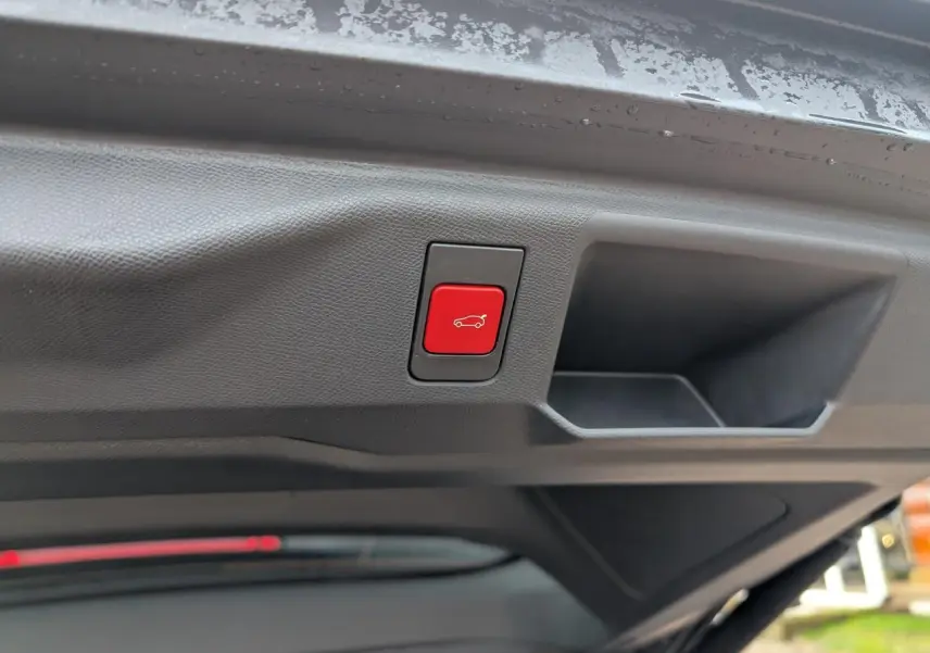 Bouton rouge d'ouverture électrique du hayon visible sous le coffre d'un Peugeot 5008 gris hybride 2025.