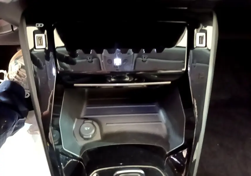 Vue plongeante sur la console centrale noire du Peugeot 2008 gris clair, avec prise 12V et rangement intégré.