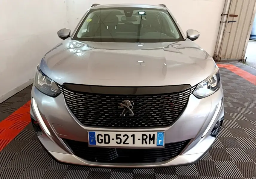 Vue avant d'un Peugeot 2008 gris clair 2021 avec calandre noire et feux LED allumés en intérieur.
