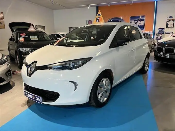 Renault ZOE R90 Life blanc glacier vue 3/4 avant droit en showroom avec logo Distinxion visible.