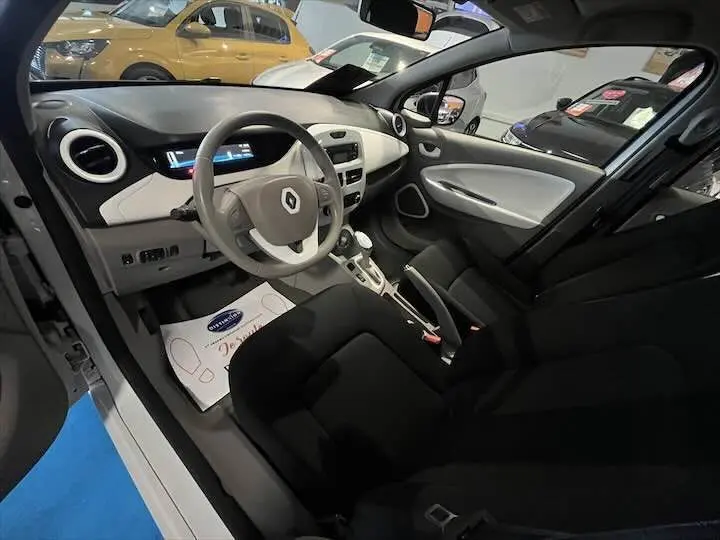 Intérieur de Renault ZOE blanc glacier, vue côté conducteur montrant tableau de bord et sièges noirs.