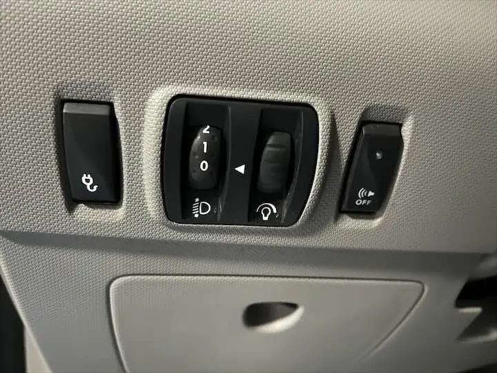 Gros plan sur les commandes de réglage des phares et des aides à la conduite dans une Renault ZOE blanc glacier.