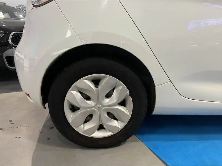 Gros plan sur la roue arrière gauche d'une Renault ZOE blanc glacier, mettant en valeur la jante au design moderne.