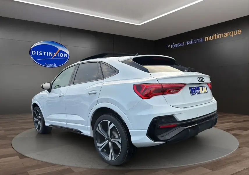 Audi Q3 Sportback blanc vue 3/4 arrière droit, jantes noires brillantes et toit panoramique en showroom.