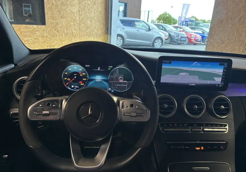 Vue intérieure centrée sur le volant cuir multifonction et l'écran tactile GPS de la Mercedes Classe C Break noir métal.