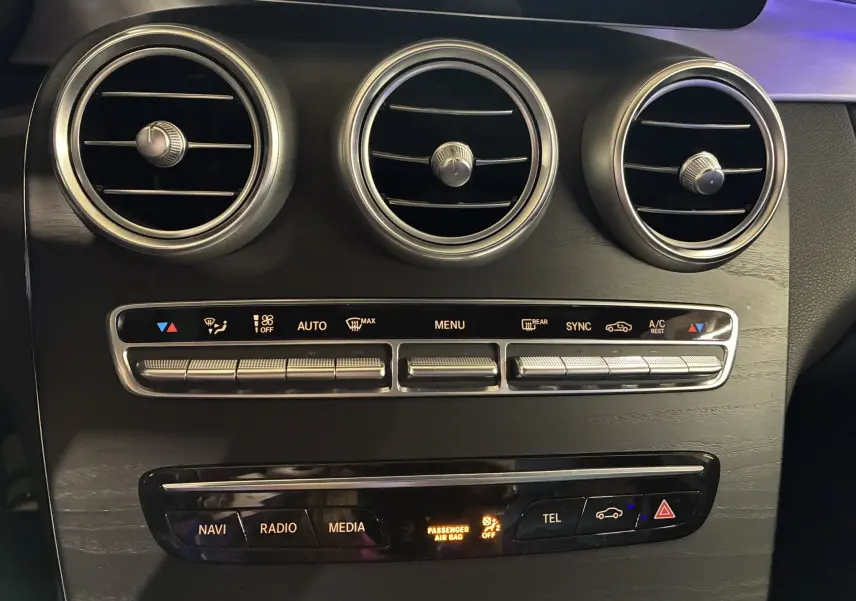 Détail du tableau de bord noir avec trois aérateurs ronds et commandes climatisation d'une Mercedes Classe C Break AMG Line 2021.
