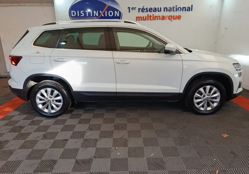Vue de profil côté gauche d'un Skoda Karoq blanc 2024 dans un showroom avec sol à damiers noirs et rouges.