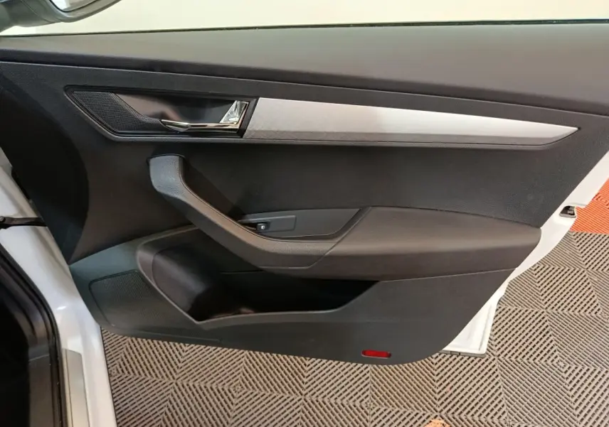 Vue intérieure côté gauche de la porte avant blanche du Skoda Karoq 2024 avec garniture noire et insert argenté.