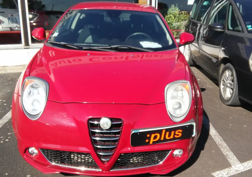 Vue avant d'une Alfa Romeo MiTo rouge vif avec calandre caractéristique en V et phares ronds, stationnée en extérieur.