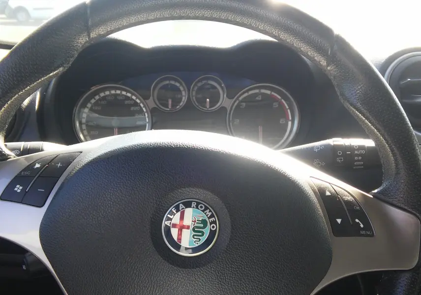 Vue rapprochée du volant en cuir noir d'une Alfa Romeo MiTo 2010 avec tableau de bord et commandes intégrées visibles.
