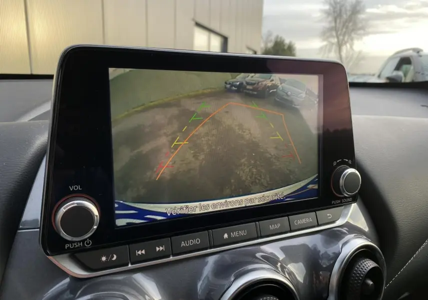 Écran tactile du Nissan Juke blanc perle 2024 montrant la caméra de recul avec lignes d’aide au stationnement.