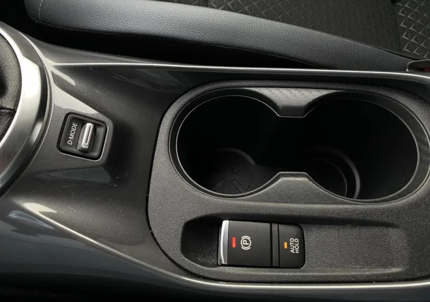 Gros plan sur la console centrale noire du Nissan Juke blanc perle, avec bouton frein électrique et porte-gobelets.