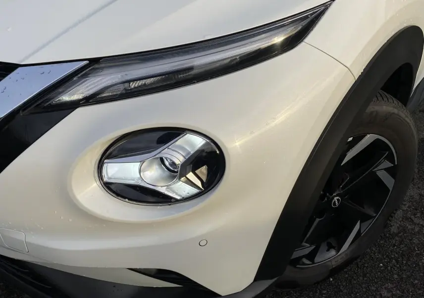 Gros plan sur le phare avant droit et la jante noire du Nissan Juke blanc perle 2024, version N-Connecta.
