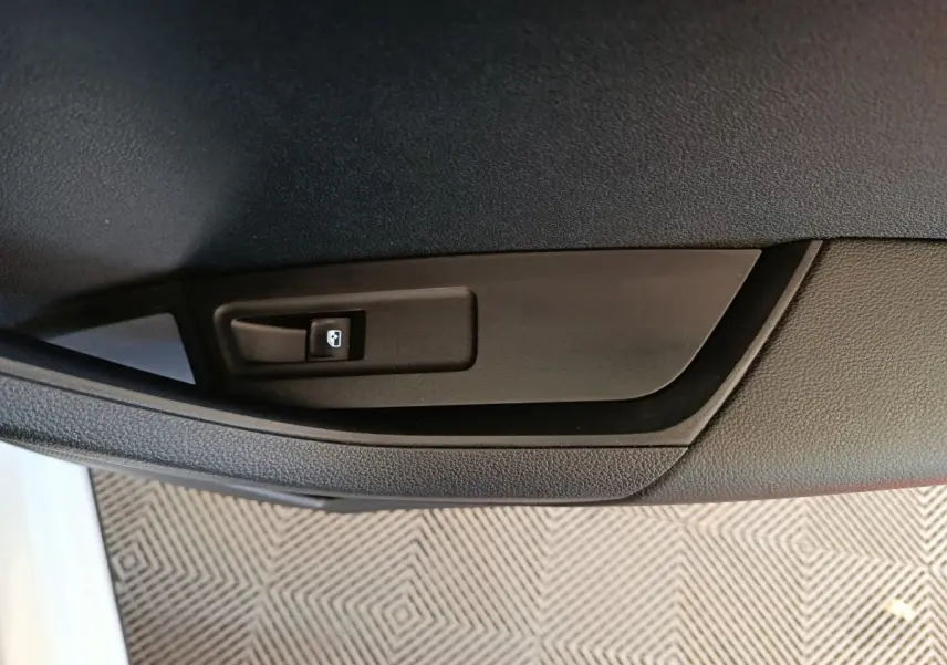 Gros plan sur la commande de lève-vitre arrière droite dans l’habitacle noir d’un Skoda Karoq blanc 2024.