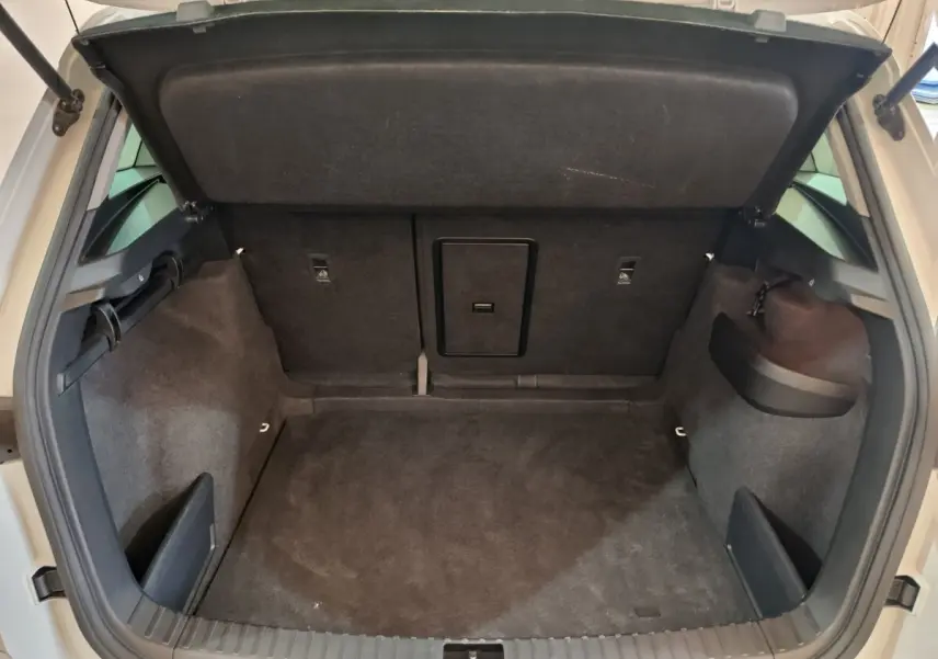 Coffre ouvert vu de l'arrière d'un Skoda Karoq blanc 2024, espace de chargement avec banquette rabattable et trappe à ski.