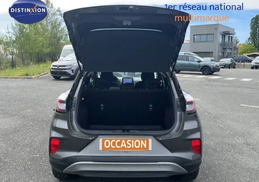 Vue arrière d'un Ford Puma gris 2021 avec coffre ouvert, mettant en valeur l'espace de chargement et les feux arrière.