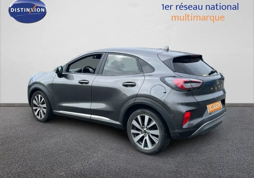 Ford Puma gris en vue 3/4 arrière côté gauche, avec jantes alliage et feux arrière distinctifs.