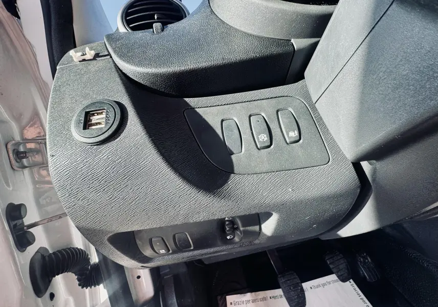 Vue rapprochée de la console côté gauche du Renault Kangoo blanc, montrant les boutons de commande et une prise USB double.